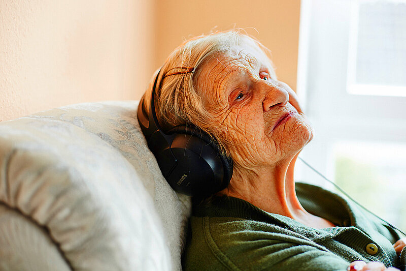 alte Frau mit Kopfhörern sitzt im Sessel